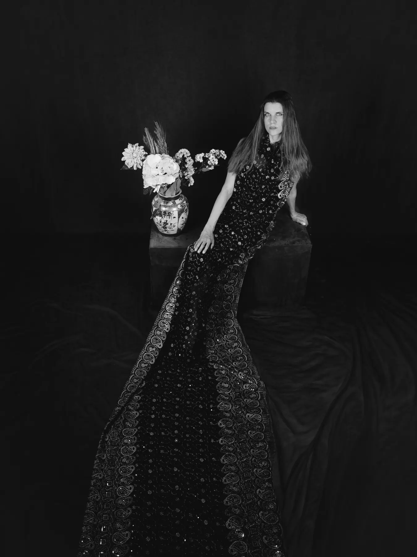 Sophie Duvent in einem langen gemusterten Kleid neben einer Blumenvase